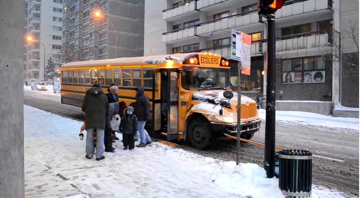 Students boarding a yellow school bus in light snowfall, showing school still open during mild winter weather
