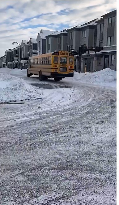 School bus driving down a snow-covered residential street during a winter storm